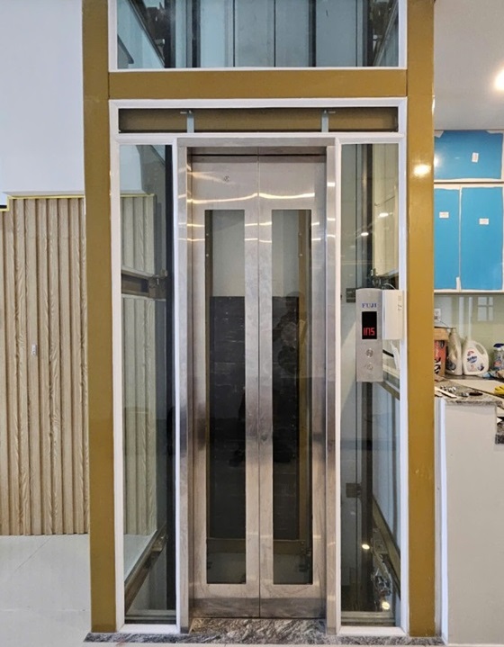 Thang máy homlift khung thép sơn vàng vách kính trắng khung bao bản rộng vuông