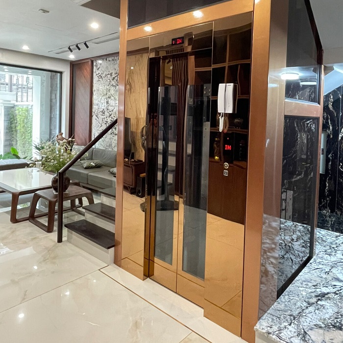 Thang máy khung thép sơn tĩnh điện vàng vách kính đen cửa inox vàng gương khung bao bản rộng